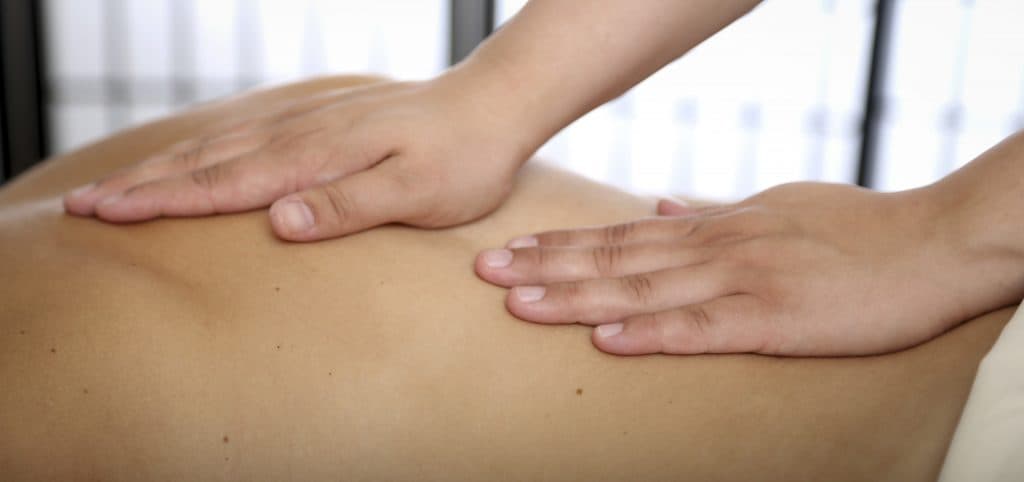 A therapist's hands giving broad relaxation strokes across a client's back