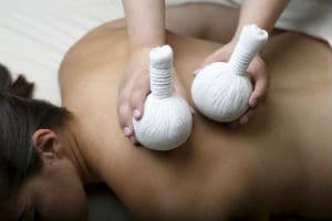 A therapist pressing warm herbal compress balls into a client's back